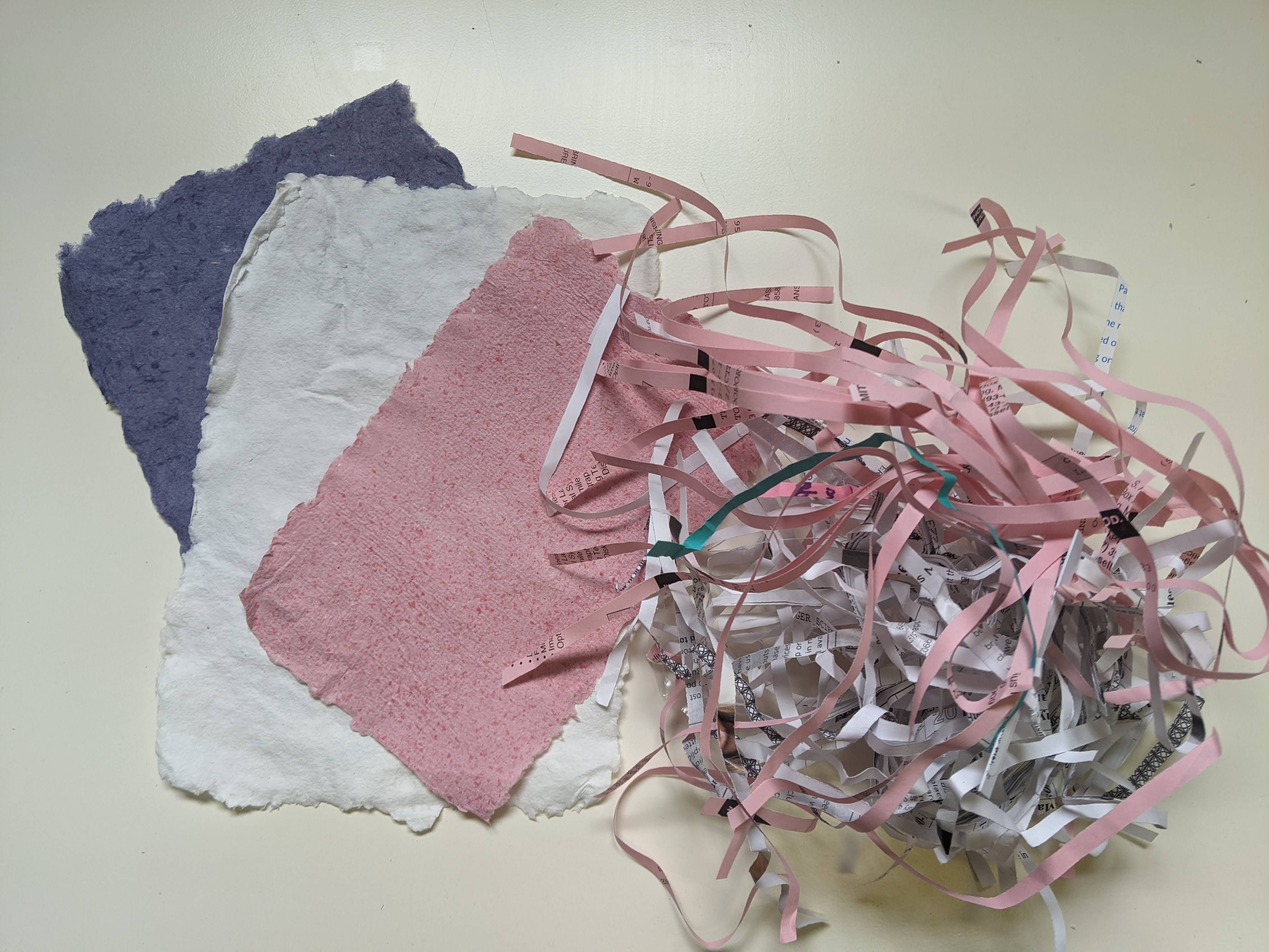 three pieces of handmade paper, with a bundle of shredded paper.